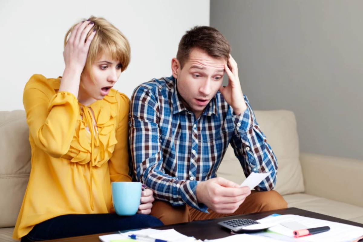 uomo e donna seduti sul divano disperati mentre leggono le bollette