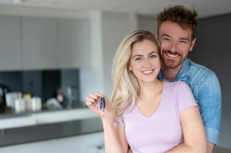 donna che sorride con delle chiavi in mano e uomo che la abbraccia da dietro